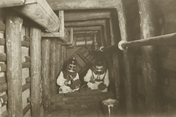 Foto von zwei Bergleuten mit Rauchhelmen, die in einem Übungsstollen eine Mauer bauen.