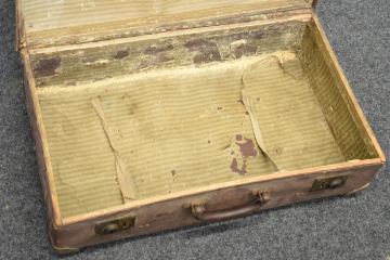 Ein alter Koffer, der aufgeklappt und leer auf einem Teppichboden steht. 