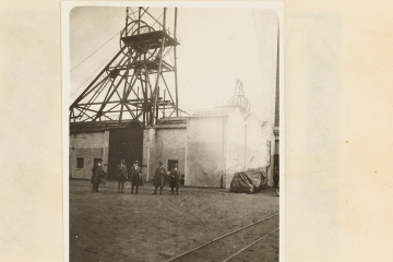 Gruppenfoto mit fünf Männern vor einem Gebäude mit Fördergerüst, im Hintergrund weitere Anlagen, im Vordergrund Gleise