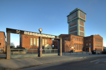 Eine Werkshalle mit Eingangstor und im Hintergrund ein gemauerter Förderturm