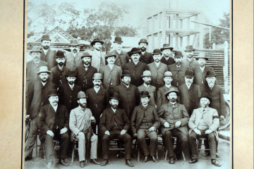 Gruppenfoto stehende und sitzende Männer draußen vor einer Ausstellung